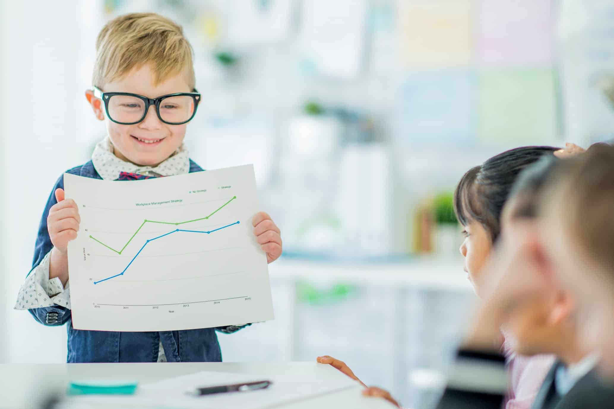 Young boy with glasses holding a piece of paper with a graph on to 2 classmates