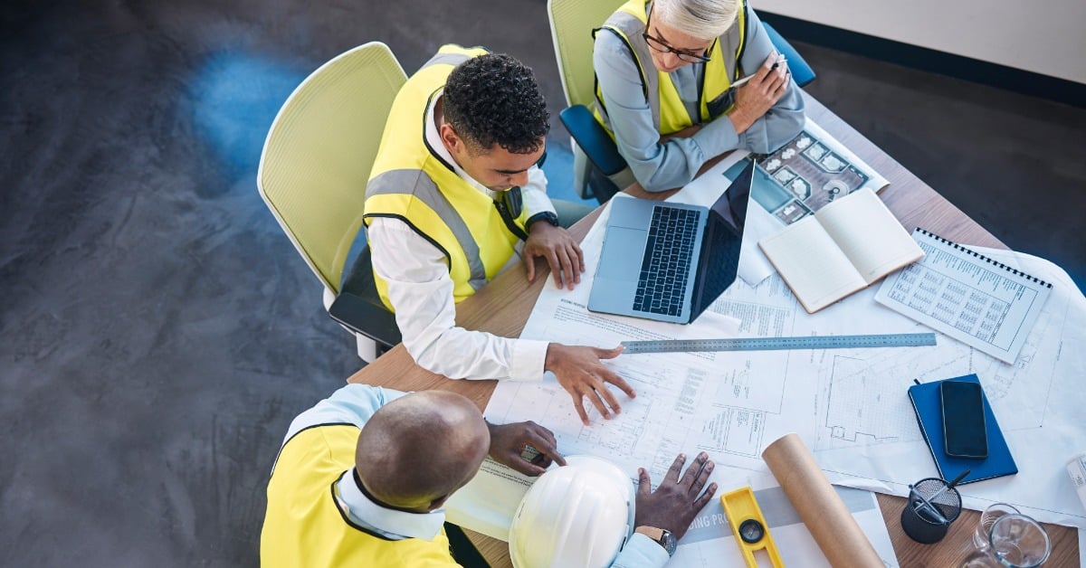3 people in high-vis vests sat around a table strewn with building plans